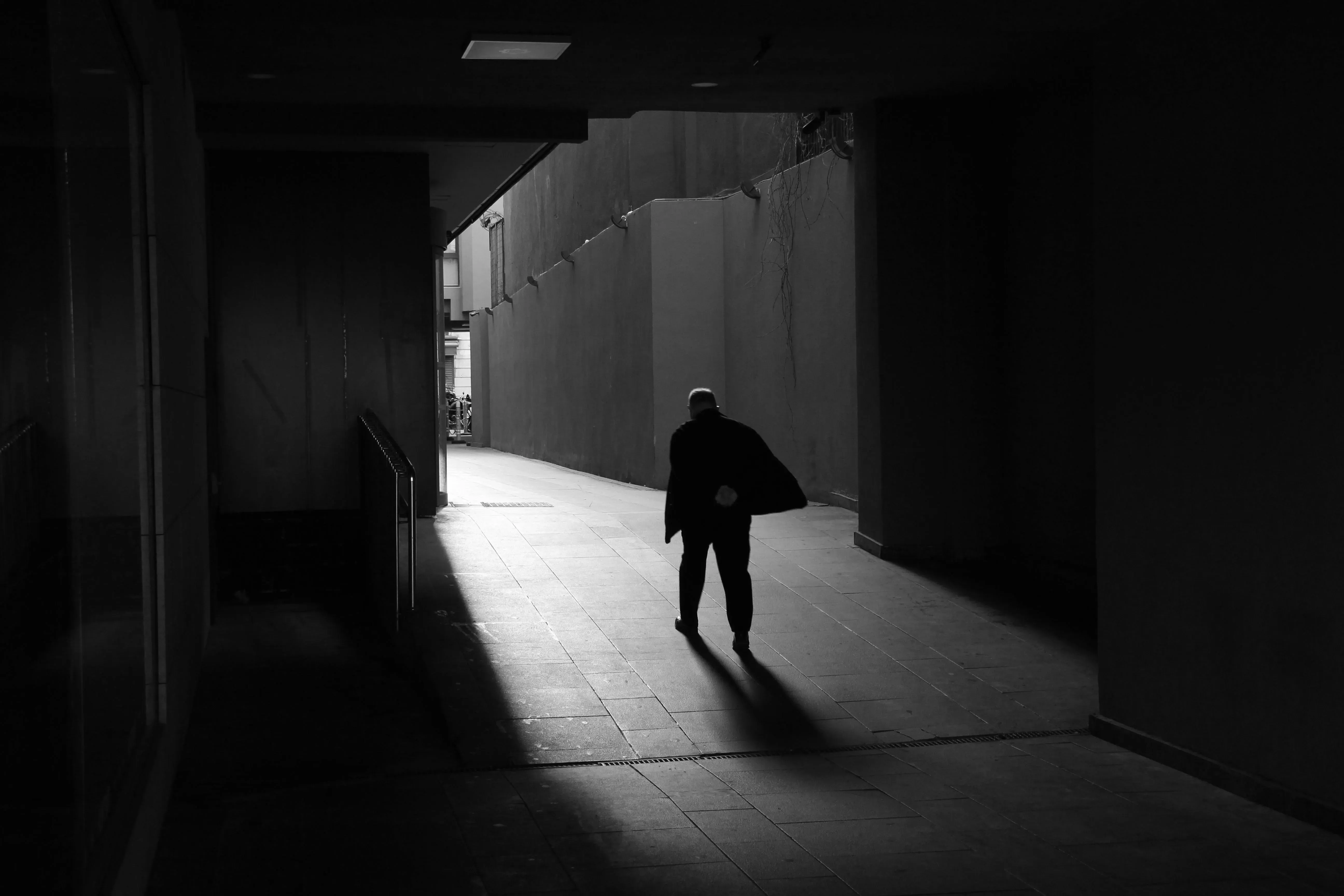 Photographie en noir et blanc d'une personne marchant dans un rayon de lumière traversant un grand espace sombre.